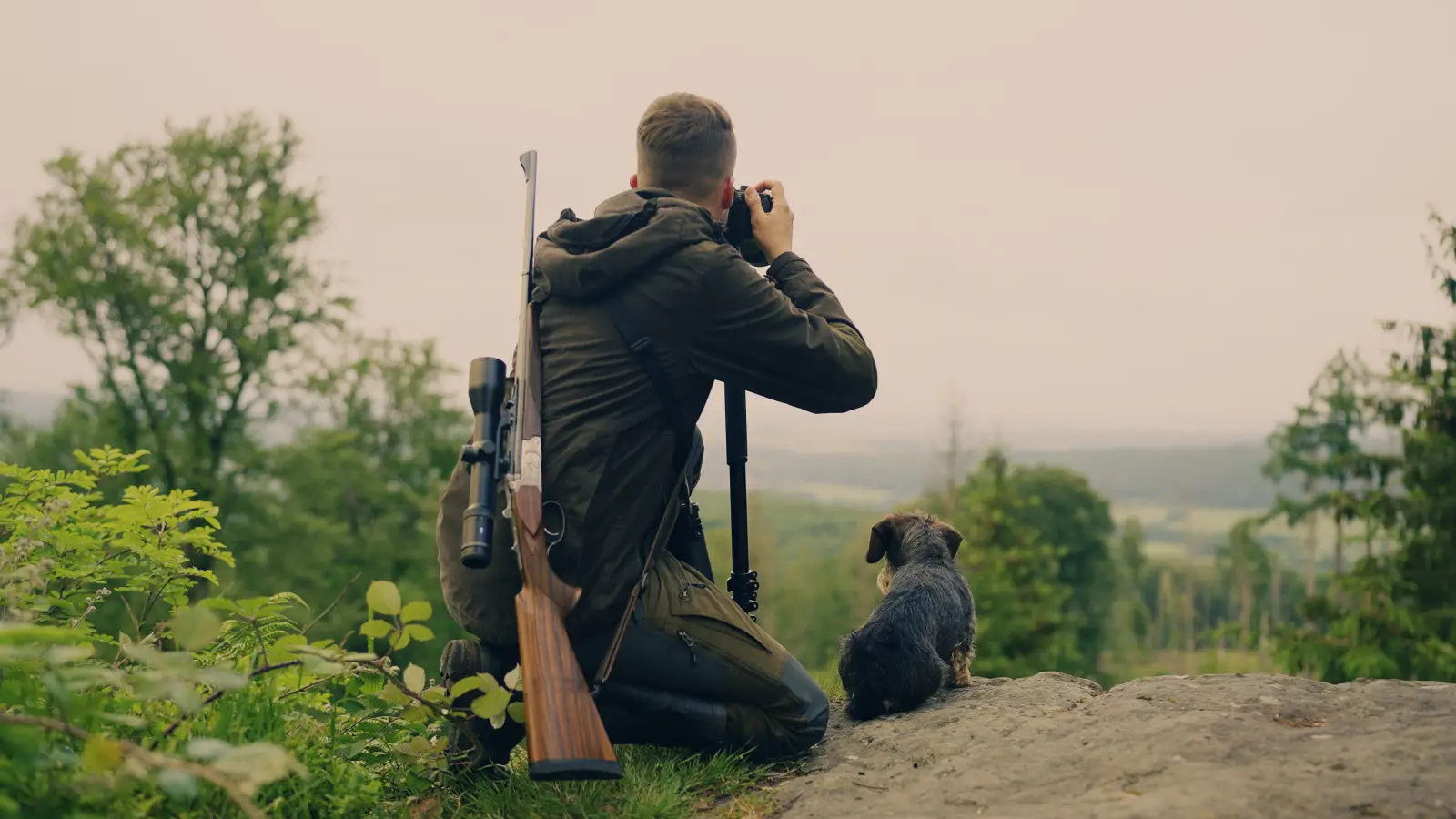 Jäger mit Jagdhund blickt über ein weites Tal